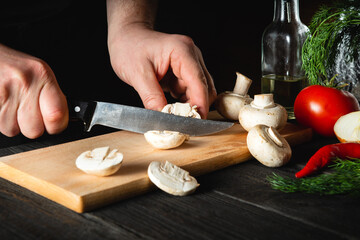 The chef cuts mushrooms with knife to prepare delicious food. Set of vegetables on a vintage...