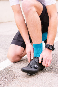 Crop unrecognizable male bicyclist in sports clothes and modern cycling shoes squatting on roadway against bike