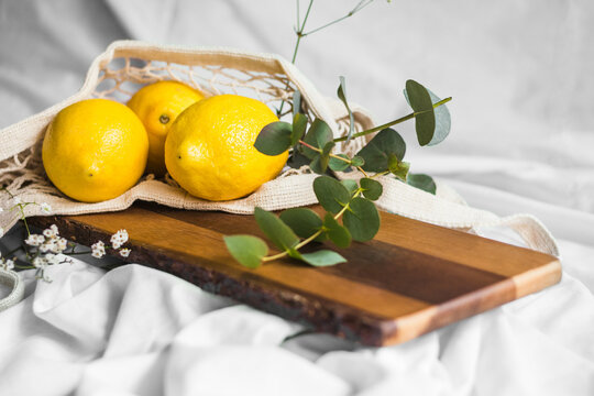 Colorful whole lemons in zero waste bag near wavy plant sprig on wooden chopping board on creased textile