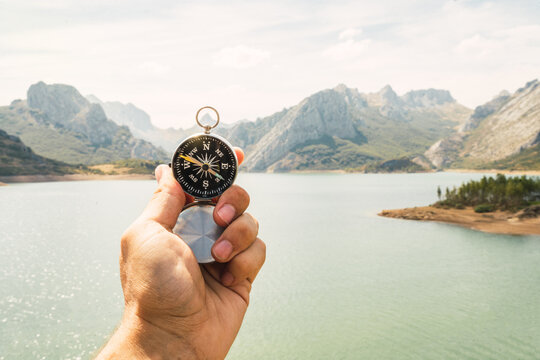 Closeup of a hand holding a compass in a magnificent landscape with river and mountains