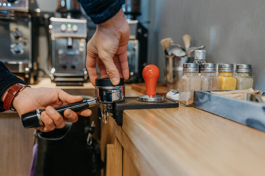 Crop faceless barista standing at table and preparing fresh aromatic coffee while working in cafeteria in daytime