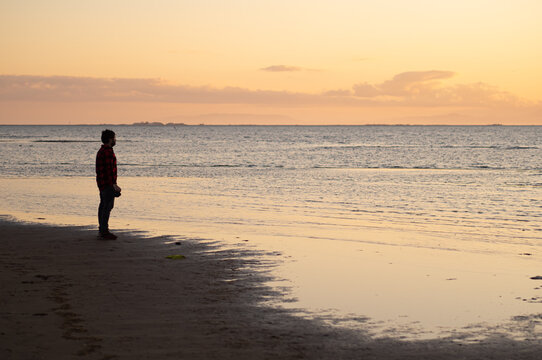 Side view of male traveler with photo camera standing contemplating seashore at sunset time