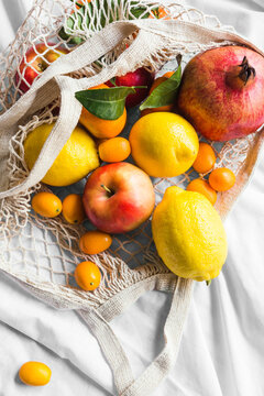 From above of different whole ripe apple with lemons near pomegranate and kumquats in eco bag on creased cloth