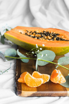 Half of pawpaw with seeds between tangerines and cumquats with leaves on white crumpled cloth