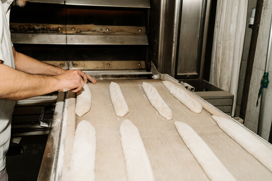 Side view of crop anonymous male baker cutting raw bread dough creating ornament on soft surface at work