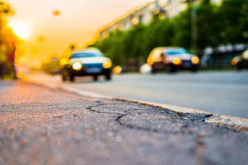 Sunset in the city, two cars driving on the road. Close up view from the sidewalk level