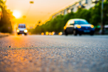Fototapeta na wymiar Sunset in the city, the cars driving on the road. Close up view from the asphalt level