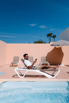 Side view of male freelancer lying on lounger at poolside and surfing Internet on mobile phone during telework in summer on sunny day