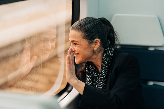 Side view of positive female waving hand and looking out window while sitting on passenger seat in wagon during ride