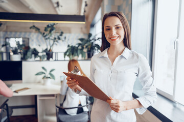 Portrait of a young attractive businesswoman holding clipboard in office