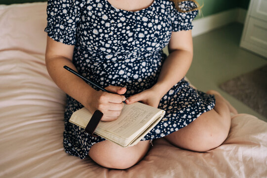 Crop pregnant woman sitting on bed and writing notes