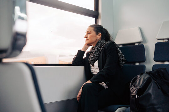 Side view of middle aged female with closed eyes leaning on hand while sitting on passenger seat during ride in wagon looking outside through the windows