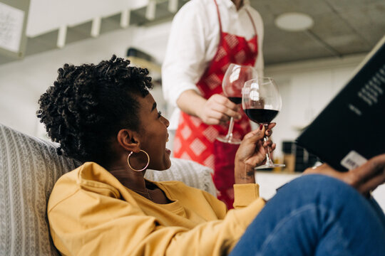 Low angle of multiracial couple clicking glasses with red wine while enjoying weekend at home