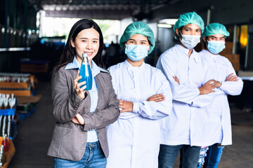 Portrait images of Asian attractive woman factory manager showing quality of basil water bottle with blur staff background, to people and Industrial plant Beverage products Export standard concept.