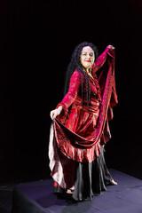 Obraz premium Gypsy woman barefoot with long black hair dances in a red dress on a black background.