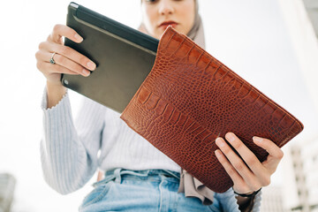 From below of crop ethnic female in headscarf standing with laptop and leather case in street