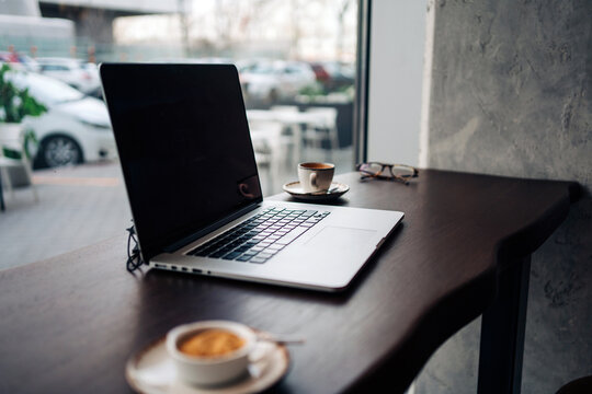 Modern netbook with black screen on wooden table with cups of aromatic coffee in cafeteria - Powered by Adobe