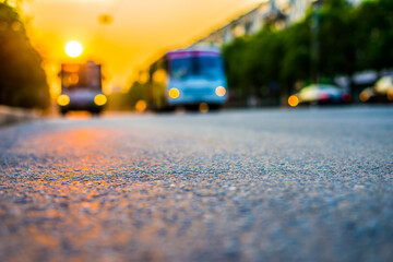 Sunset in the city, the buses driving on the road. Close up view from the asphalt level