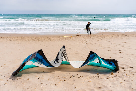 Female athlete in wetsuit touching hair on sandy beach between inflatable kite and foamy sea