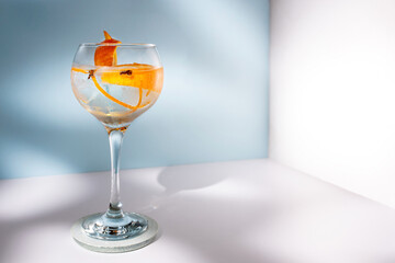 Transparent glass of highball cocktail decorated with citrus fruit zest and clove against shadows in sunlight