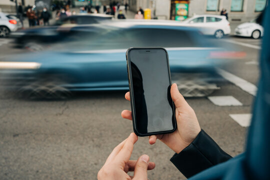Crop anonymous female standing near road with busy traffic and browsing mobile phone with black screen