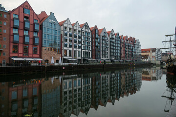A panoramic view on the shores of Martwa Wisla flowing through Gdansk in Poland. The buildings reflect in the calm surface of the river. New architecture meeting with medieval constructions. Overcast