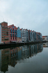 Fototapeta na wymiar A panoramic view on the shores of Martwa Wisla flowing through Gdansk in Poland. The buildings reflect in the calm surface of the river. New architecture meeting with medieval constructions. Overcast