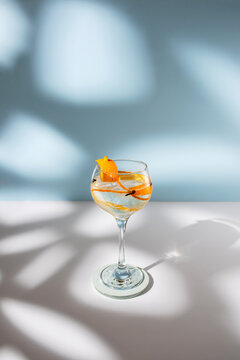 Transparent glass of highball cocktail decorated with citrus fruit zest and clove against shadows in sunlight