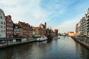 Naklejka premium A panoramic view on the shores of Martwa Wisla flowing through Gdansk in Poland, with medieval port crane. New architecture meeting with medieval constructions. Sunny day. Calm water. City tour