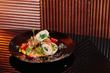 Spinach meat rolls served with asparagus, vegetables and vegetable puree on a black plate. Close-up. Space