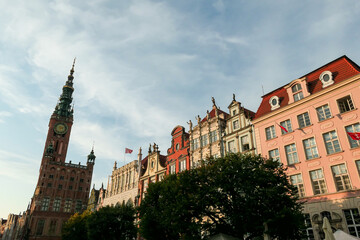 Fototapeta premium A close up of the facades of tall building in the middle of Old Town in Gdansk, Poland. The buildings have many bright colors, they are richly decorated. High tower of Town Hall. City tour. Clear day.