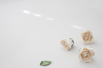 Three artificial roses laying on a neutral coloured table. Minimalist closeup with empty space for...