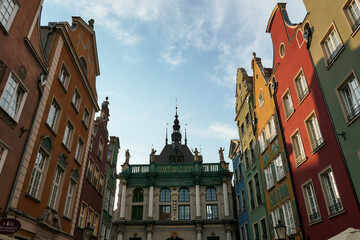 Fototapeta premium A close up of the facades of tall building in the middle of Old Town in Gdansk, Poland. The buildings have many bright colors, they are richly decorated. There is a cathedra with high towers in front