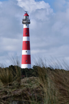 Classic, historic old red and white lighthouse with dunes and grass, sunny windy day and turbulent clouds on the Dutch island of Ameland, Hollum, April 2021