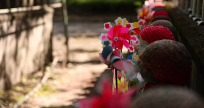 A slow motion of moving colorful windmills with Jizo statue daytime closeup