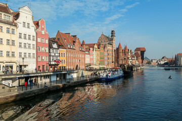 Fototapeta na wymiar A panoramic view on the shores of Martwa Wisla flowing through Gdansk in Poland, with medieval port crane. New architecture meeting with medieval constructions. Sunny day. Calm water. City tour