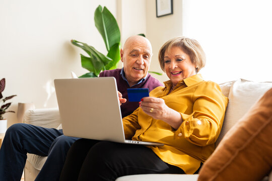 Cheerful mature couple making payment with plastic card during online shopping via laptop at home