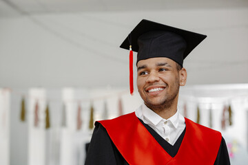Portrait of a smiling Black student, wearing a graduation gown and a square cap with a red tassel...