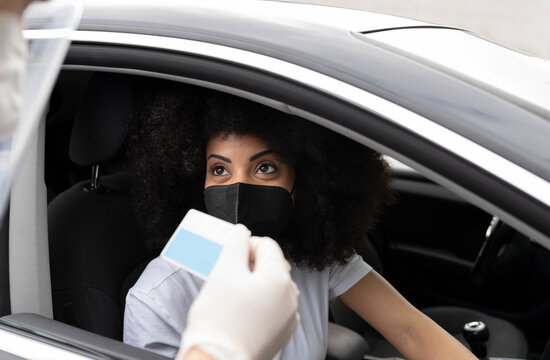 Cropped unrecognizable doctor in protective uniform, latex gloves and face shield checking African American female patient Identification card before vaccine procedure inside the car on a drive through mobile clinic during coronavirus outbreak