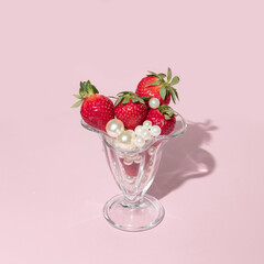 Creative concept with strawberries, white pearls  and glass jar on pastel pink background. Minimal fruit or food layout. Romantic spring or summer idea.