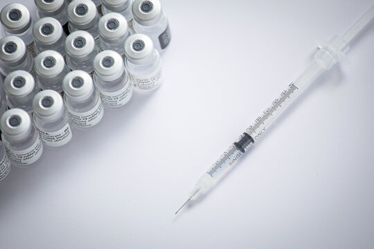 Close-up of some vials with the coronavirus vaccine along with a needle on a white background
