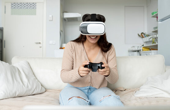 Unrecognizable cheerful female with gamepad experiencing virtual reality in goggles while playing video game on couch in house