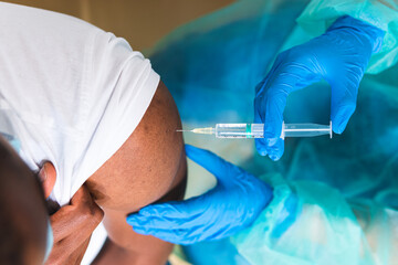 Cropped unrecognizable female medical specialist in protective uniform, latex gloves and face mask vaccinating African American man patient in clinic during coronavirus outbreak