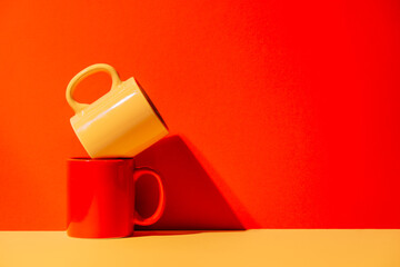 Creative colorful mugs on yellow and red background in studio