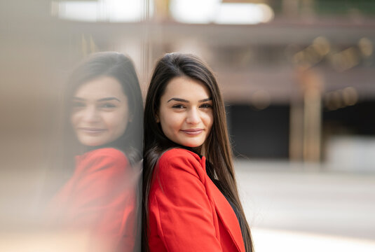 Side View Of Delighted Female In Red Jacket Leaning On Wall In City And Looking At Camera