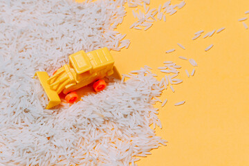 From above of small plastic toy tractor collecting pile of rice grains scattered on yellow background