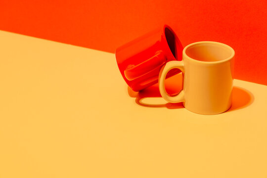 Creative colorful mugs on yellow and red background in studio