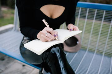 High angle of crop unrecognizable female entrepreneur sitting on bench in city and writing business plan in notebook