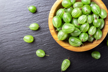 Fresh gooseberries in wooden bowl on black stone slate background.