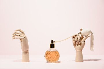 Stylish transparent bottle of perfume placed between wooden hands placed on pink background in light studio